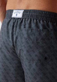 Sive kupaće gaće s ponavljajućim uzorkom logotipa, elastičnom strukom i stražnjim džepom s kopčom na pritiskanje. Vidljiva oznaka branda.