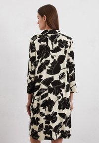 Abito a fiori in bianco e nero con maniche a tre quarti, caratterizzato da una vestibilità ampia e un tessuto morbido su sfondo beige chiaro.