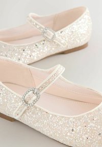 Spīdīgi balti baleta zābaciņi ar plakanu zoli un plānu siksniņu, kurai ir dekoratīva rhinestone sprādze. Mīksta, gluda iekšējā oderējums.