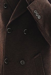 Brązowy płaszcz z mieszanki wełny, wyróżniający się teksturowanym materiałem, podwójnym zapięciem, dużymi czarnymi guzikami oraz dopasowanym kołnierzem.