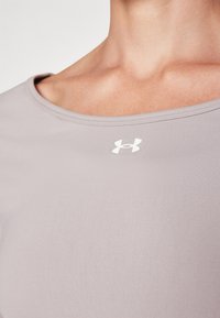 Svijetlosivi atletski top s mekom, glatkom teksturom, s širokim izrezom i bijelim logotipom na području prsa.