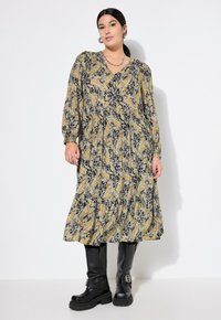 Robe longue et fluide de couleur bleu foncé avec un motif floral jaune et blanc. Présente un décolleté en V, des manches longues et une jupe à volants, associée à des bottes noires.