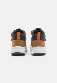 Zapatillas de ante marrón y textil azul marino con suelas blancas, con detalles en naranja y un cuello acolchado. La vista trasera muestra el cordaje y la lengüeta del talón.