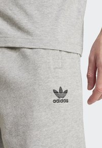 Gray cotton athletic shorts with textured fabric, featuring a black Adidas logo and a casual, straight cut. Hand partially shown.