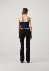 Haut sans manches en denim foncé avec une coupe ajustée, associé à un pantalon noir évasé. Le haut présente une fermeture éclair visible à l'arrière.
