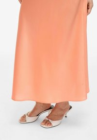 Robe maxi en satin pêche avec une texture lisse, assortie à des talons ouverts blancs avec un petit nœud décoratif et un talon courbé.