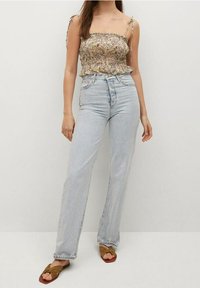 Haut léger à fleurs avec bretelles ajustables à nouer, associé à un jean bleu clair taille haute à jambes larges. Sandales plates marron complètent le look.