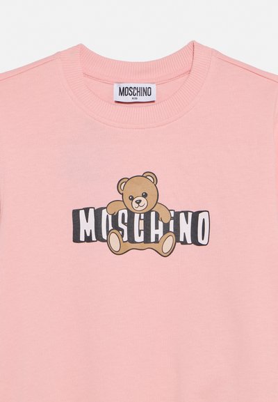 Rožinis vaikiškas džemperis su gofruota apykakle, centre pavaizduotas meškiukas, apsikabinęs juodai baltą užrašą „MOSCHINO“.