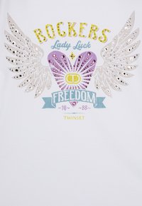 HVIT t-skjorte med et grafisk design med sølvfargede paljetter som vinger, et hjerte, og teksten "ROCKERS, Lady Luck, FREEDOM" i forskjellige farger.