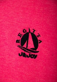 Tissu texturé rose avec un logo brodé noir représentant un voilier et le texte "REGATTA" et "J&JOY" en dessous.