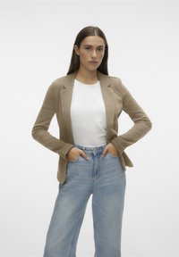 Khaki blazer with a tailored fit, single-button closure, and long sleeves, worn over a white shirt and high-waisted light blue jeans.