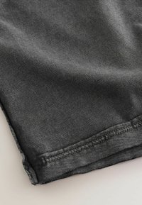 Tissu en denim gris foncé montrant un gros plan d’un ourlet à double couture avec un léger délavage et une texture subtile.