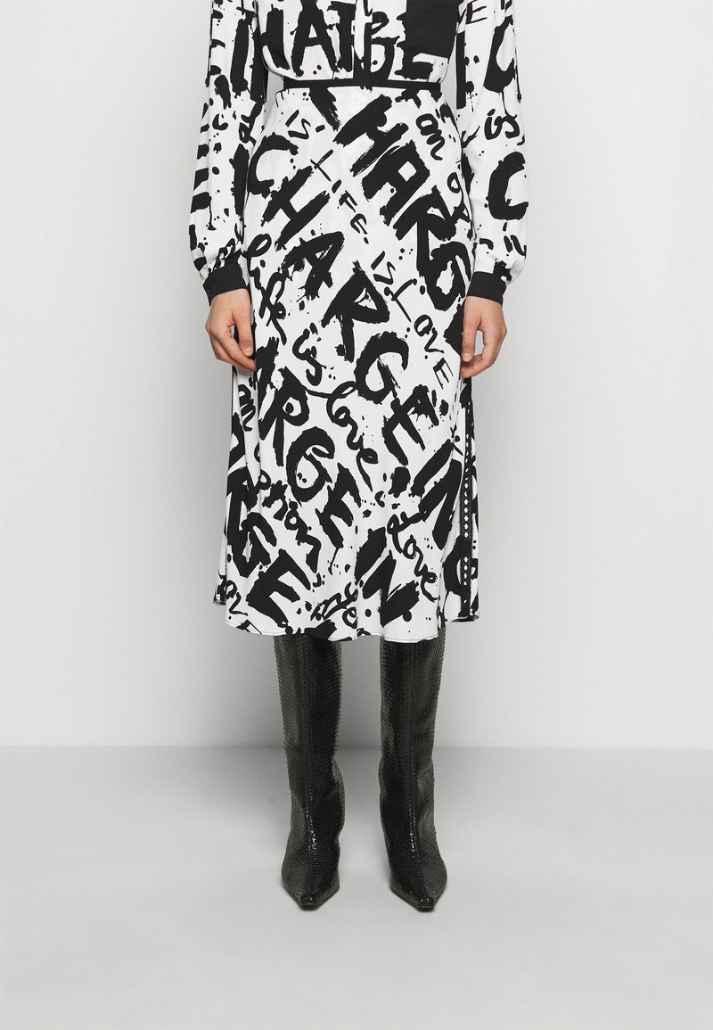 Abito in bianco e nero con motivi testuali astratti, dotato di maniche lunghe e una vestibilità ampia, abbinato a stivali neri alti fino al ginocchio di texture.