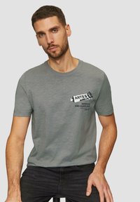 Hallid hall puuvilla T-särk lühikeste varrukatega, millel on musta värvi prinditud kujundus tekstiga "KUNSTID" ja "TEENUSED JA TARVIKUD".