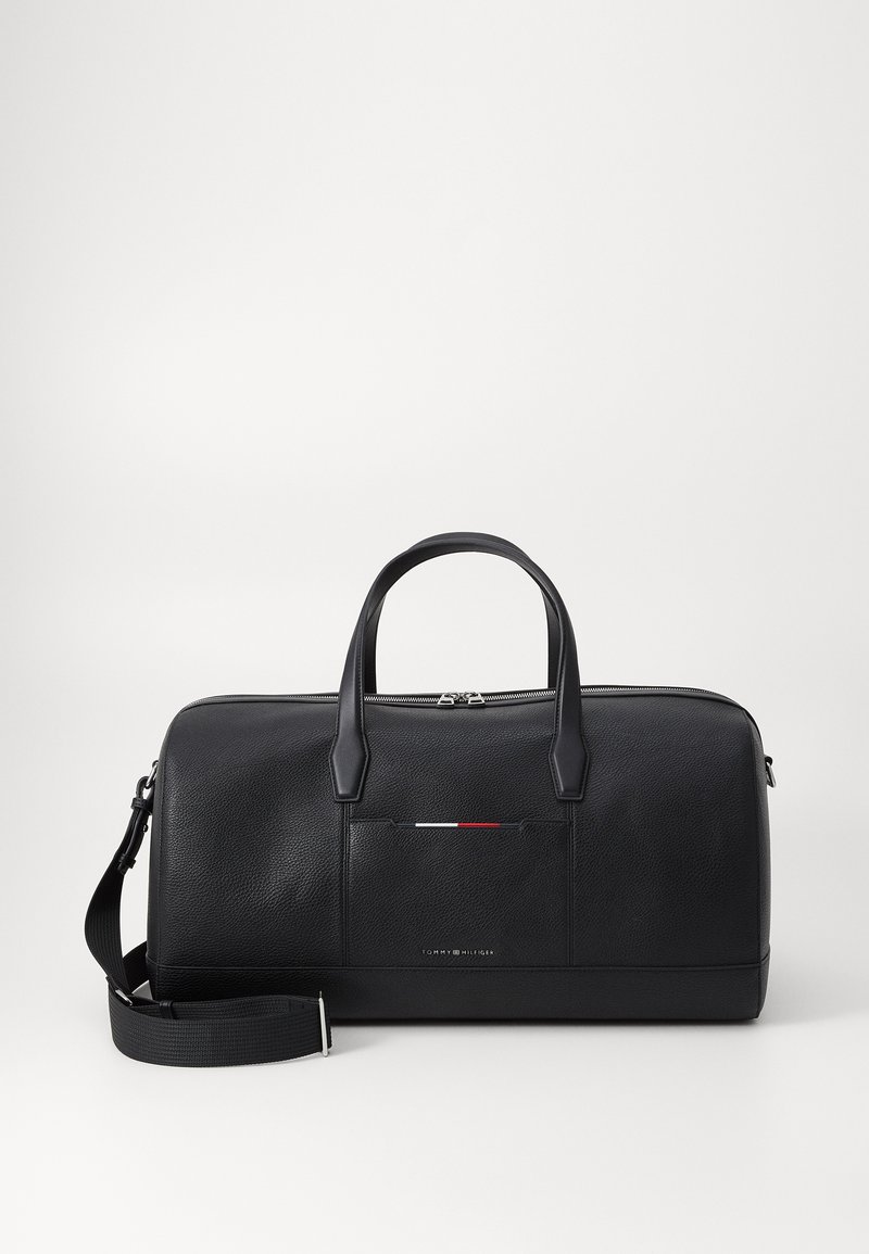 Sac de voyage en cuir noir avec surface texturée, doubles poignées supérieures, sangle réglable et détails accentués à l'avant en blanc, rouge et bleu.
