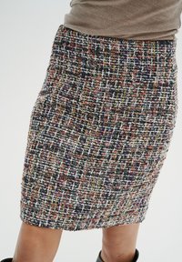 Falda lápiz tejida con un patrón de sarga multicolor, que presenta una mezcla de hilos morados, naranjas, amarillos y blancos. Acabado texturizado.