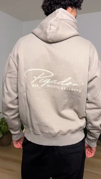 Light beige hoodie with a large, centered white logo on the back reading "Pegadon ALL RIGHTS RESERVED," featuring a drawstring hood and ribbed cuffs.