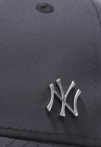 Námornická čepice vyrobená z hladké tkaniny s kovovým stříbrným logem New York Yankees vepředu. Kulatá horní část s texturovaným knoflíkem.