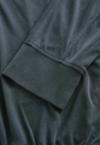 Gros plan d'un poignet de chemise à manches longues gris foncé avec coutures visibles et texture de tissu doux.