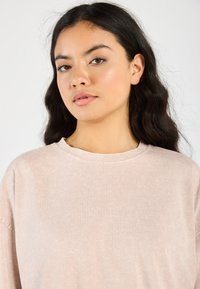 Lys rosa, oversized bomullsgenser med rund hals og lange ermer. Myk tekstur, subtil glans og minimale sømdetaljer.