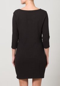 Muotoutuva musta ribbineulottu mekko, jossa on kolmivartiset hihat, veneenmuotoinen pääntie ja sileä pinta. Selässä hienovaraiset saumat.