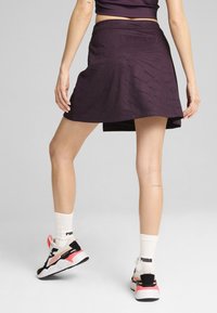 Jupe violette à motif texturé, longueur genou avec une taille élastique, associée à des chaussures de sport noires et roses et des chaussettes blanches.