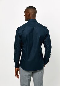 Marineblauw overhemd met lange mouwen, met een gladde textuur en een getailleerde pasvorm, voorzien van een kraag en knoopmanchetten.