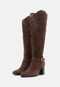 Pruunist nahast üle-põlve kingad, millel on kitsas varvas, paks konts ja reguleeritav rihm kuldse klambriga. Sile sisevooder.