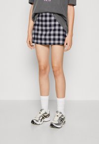 Námořnická kostkovaná mini sukně s bílými pruhy, kombinovaná s volným šedým tričkem a stříbrnými sportovními teniskami. Viditelné bílé ponožky ke kotníkům.