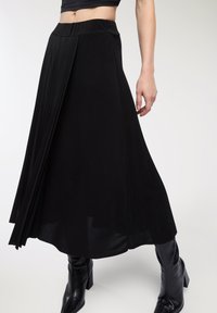 Gonna nera plissettata con una texture liscia, dotata di una vita aderente e un design fluido, abbinata a stivali neri alti con tacco.