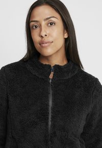 Schwarze Fleecejacke mit einer strukturierten, flauschigen Oberfläche. Verfügt über einen hohen Kragen, einen Frontreißverschluss und seitliche Taschen. Einfaches, funktionales Design.