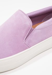 Baskets à enfiler en daim violet avec semelle en caoutchouc blanche et soufflet élastique sur le côté pour un enfilage facile.