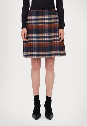 Uld ternet nederdel med nuancer af marineblå, brun og creme, med en udvidet pasform og en glat tekstur. Kombineret med sorte ankelstøvler.