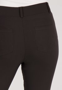 Zwarte, strakke broek met een gladde textuur, met een middelhoge tailleband en twee achterzakken met subtiele stikseldetails.