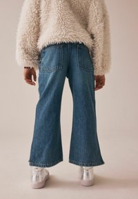 Vida byxbukser i blå denim med en blekt finish, utrustade med två bakfickor; kombinerat med en fluffig creamfärgad tröja och silverfärgade sneakers.