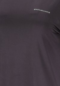 Tumma harmaa kangas, jossa ylhäällä oikeassa kulmassa on valkoisella painettu sana "KESTÄVYYS".