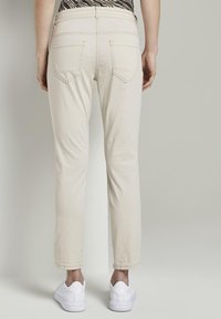 Beige Slim-Fit-Hosen mit Gesäßtaschen, kombiniert mit weißen Sneakers. Glatte Textur und einfaches Design, mit einem sauberen Saum.