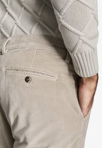 Beige corduroy bukser med ribbet tekstur, med baglommer og en knapdetalje, parret med en lys grå tekstureret striktrøje.