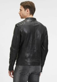 Giacca di pelle nera con design aderente, caratterizzata da dettagli a coste sulle spalle e polsini con zip, texture liscia e cuciture angolari.