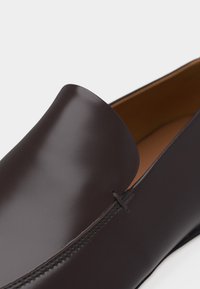 Σκούρο καφέ δερμάτινο μοκασίνι με λείο φινίρισμα και ορατή ραφή κατά μήκος της κορυφαίας ακμής.