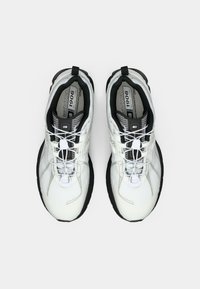 Un paio di scarpe sportive New Balance 1906 bianche e nere con lacci a rilascio rapido, viste dall'alto su uno sfondo bianco.