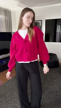 Κόκκινη πλεκτή ζακέτα με φουσκωτά μανίκια και τρία διακοσμητικά κουμπιά, φορεμένη πάνω από άσπρο πουκάμισο, σε συνδυασμό με μαύρο παντελόνι φαρδιάς γραμμής.