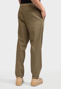 Khaki trousers with a straight fit, made of smooth fabric, featuring back pockets, rolled cuffs, and paired with beige sneakers.