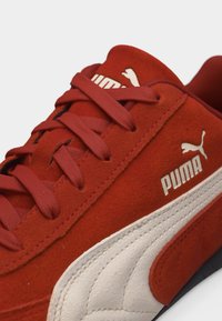 Κόκκινο σουέντ αθλητικό παπούτσι Puma με λευκό λογότυπο Puma και παχύ λευκό ρίγα στη πλευρά, με ταιριαστά κόκκινα κορδόνια και ραφές.