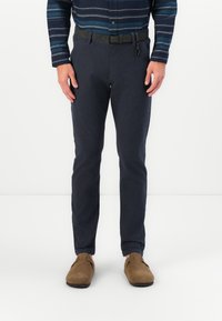 Tengeri kék pamut nadrág, slim fit szabással, fekete csattal ellátott övvel, barna velúrbőr slip-on cipőkkel párosítva.