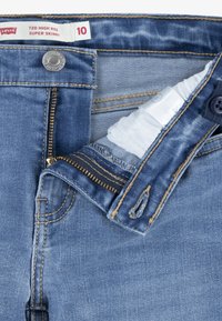 Vaqueros de tiro alto y super ajustados de Levi's en un lavado azul medio. Presentan un botón metálico, cremallera y costuras en dorado contrastante. Etiqueta de tamaño visible.