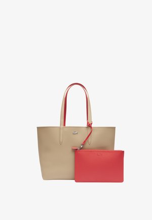 Beige leren tote bag met rode accenten, voorzien van lange handvaten en een afneembare rode ritszak. Logo-detail aan de voorkant.