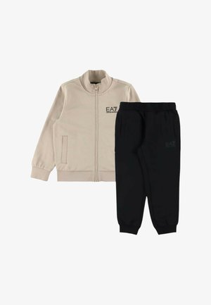 Giacca beige con zip e due tasche, pantaloni jogger con vita elastica nera, entrambi con loghi EA7 Emporio Armani discreti.
