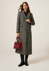 Cappotto lungo bianco e nero a motivo houndstooth con due tasche anteriori, chiusura con bottoni e rever a punta. Abbinato a una borsa bordeaux e stivali neri fino al ginocchio.