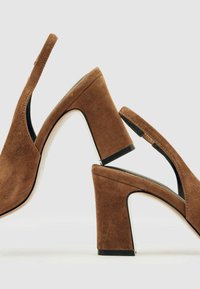 Smeđe antilop cipele s visokom potpeticom i otvorenom petom, s čvrstom potpeticom i kontrastnim bijelim naglaskom na osnovi potpetice.